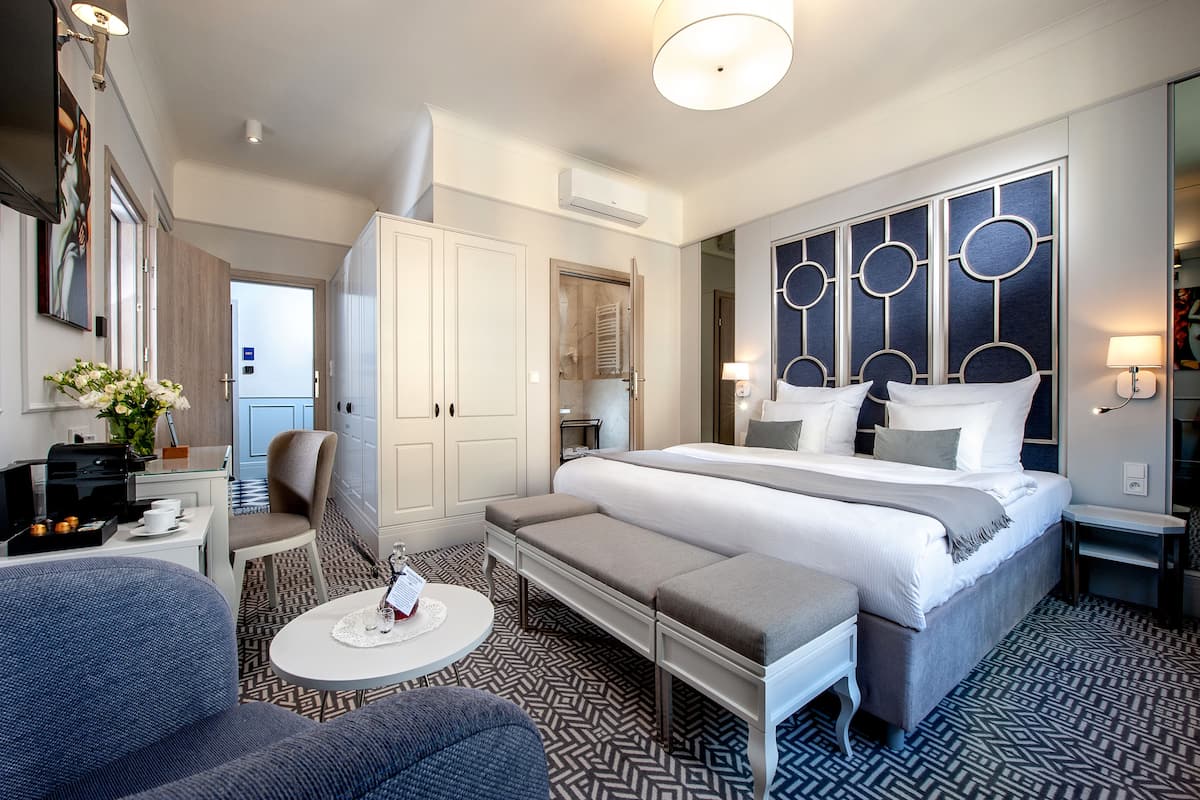 Una habitación de hotel moderna con una cama grande, una zona de estar, una mesita y un armario.