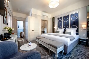 A modern hotel room with a large bed, a seating area, a small table, and a wardrobe.