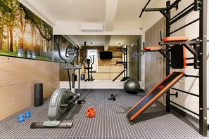 Un gimnasio en casa con equipo de ejercicio, una cinta de correr, pesas y un televisor instalado en la pared.