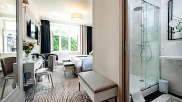 Ein Hotelzimmer mit einem Bett, einem Schreibtisch, einem Stuhl, einer Bank, einer Dusche und einem Badezimmer mit Spiegel.