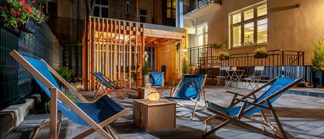Un área de estar al aire libre con sillones y una mesa central, rodeada por un edificio con balcones y ventanas.