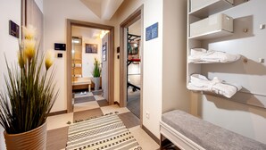 A hotel hallway with a checkered floor, a potted plant, a bench, and storage shelves with folded towels. - Amber Design Residence (Kraków)