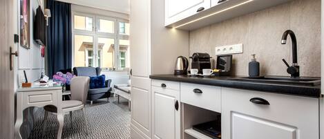 A modern kitchen with white cabinets, a black countertop, and a window with blue curtains.