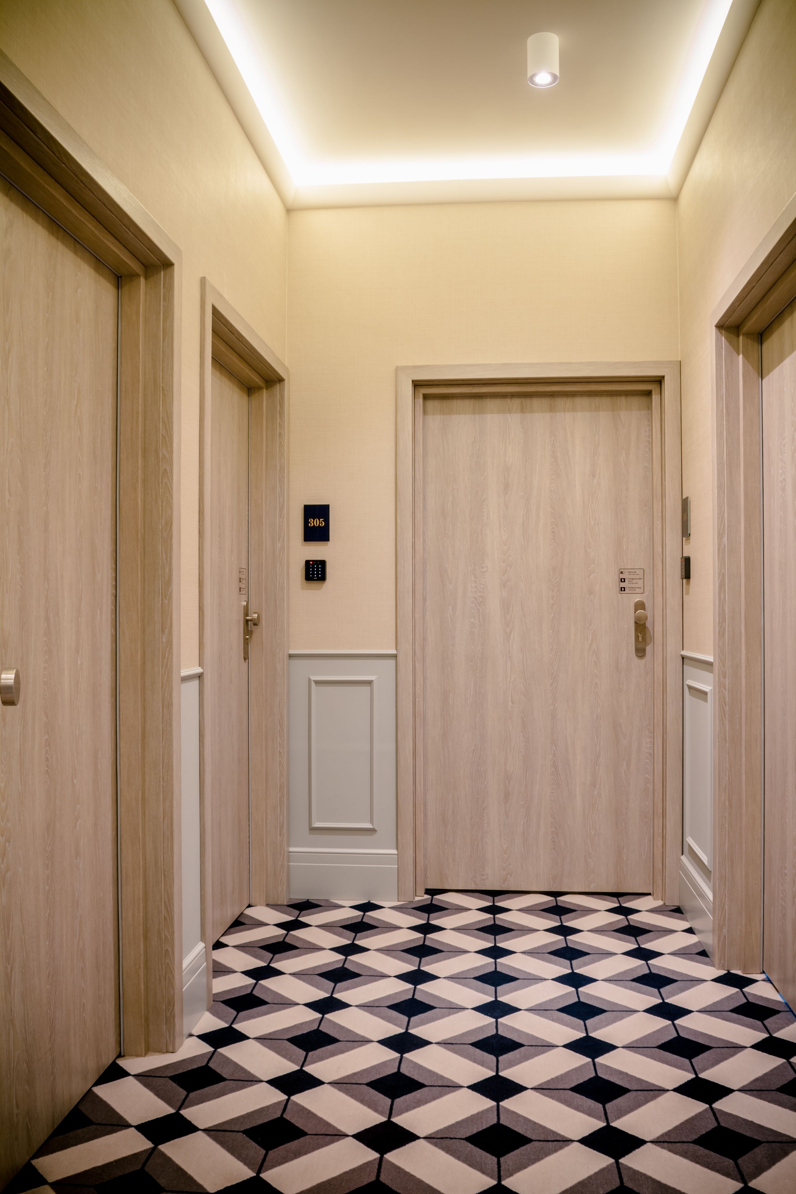 A hallway with a geometric patterned floor, wooden doors, and a ceiling light.