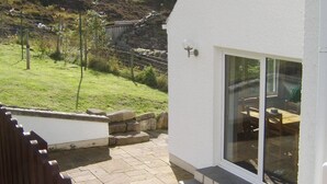 A patio area with stone flooring, a white wall, and a glass door leading to an outdoor dining area. - Top House (Ullapool)