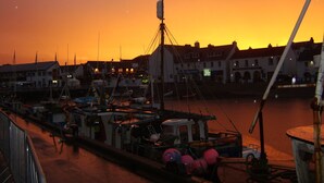 A marina at sunset with boats docked, a crane, and buildings in the background. - Top House (Ullapool)