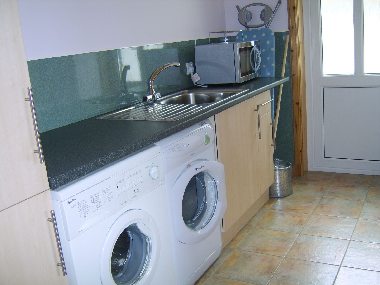Een kleine keuken met een wasmachine, een magnetron en een spoelbak.