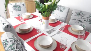 A dining table set with plates, glasses, and cutlery, surrounded by chairs with floral upholstery. - Huku Kwetu - Chelsea Garden (Dunstable)