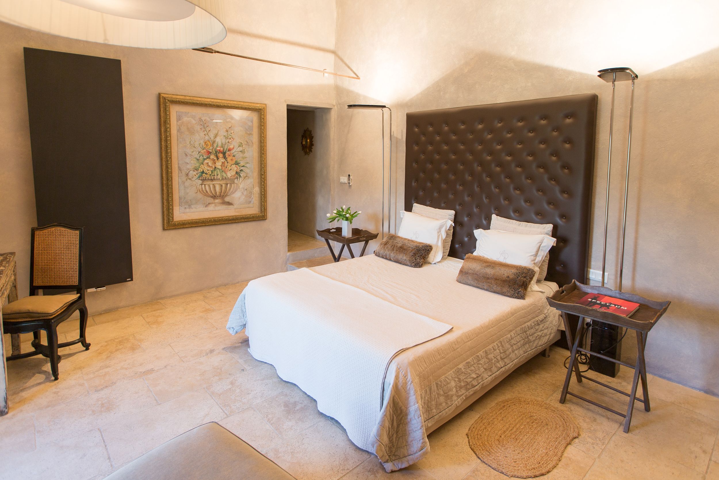 A spacious bedroom with a large bed, a bedside table, a chair, and a framed artwork on the wall.