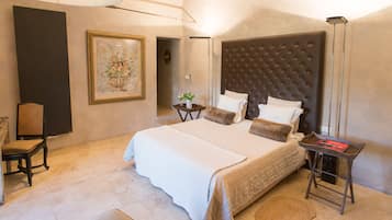A spacious bedroom with a large bed, a bedside table, a chair, and a framed artwork on the wall.