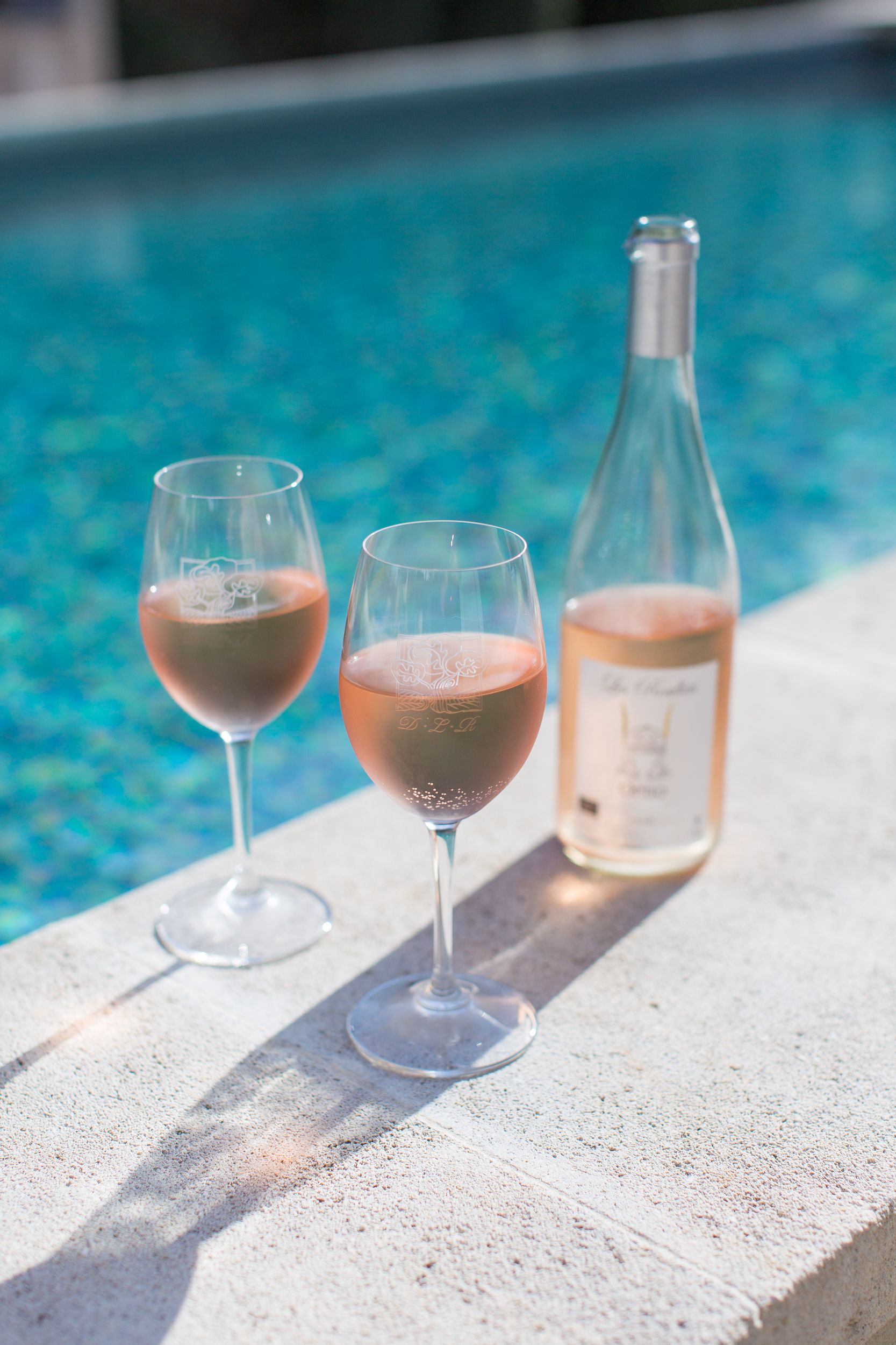 Two wine glasses and a bottle on a poolside ledge.