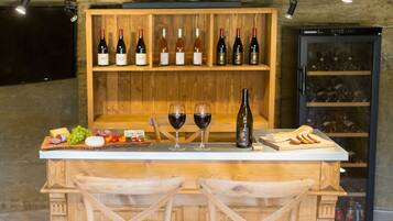 Uma área de bar em madeira com espaço para exibição de vinhos, duas taças de vinho tinto e uma tábua de queijos.