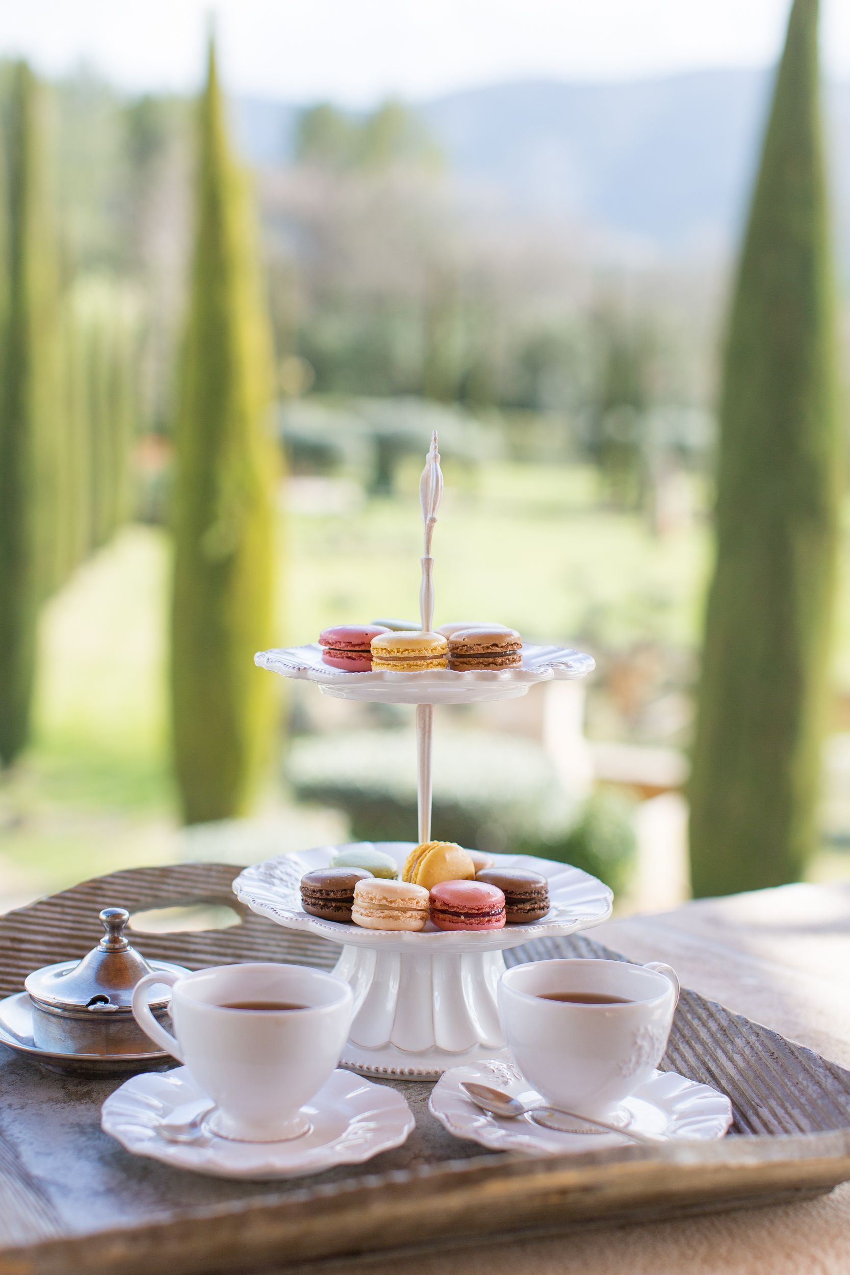 A tiered dessert stand with macarons and a cup of coffee on a tray.