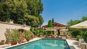 A swimming pool with lounge chairs and umbrellas, surrounded by potted plants and trees. - Domaine Les Roullets (Oppede)