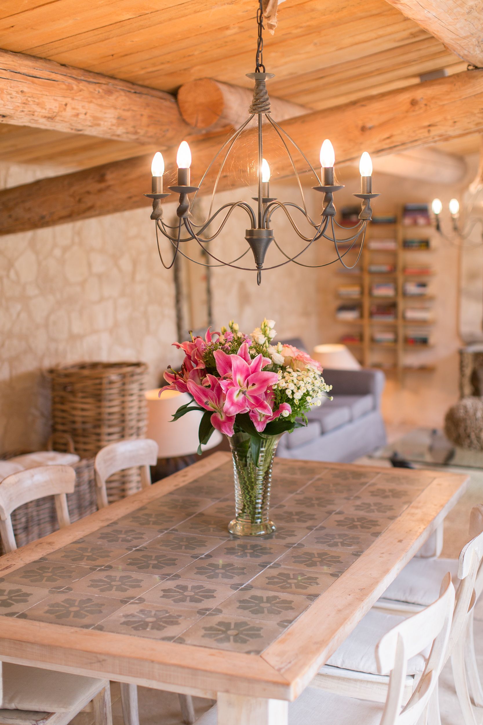 Un comedor con una mesa de madera, sillas blancas, una lámpara de araña y un jarrón de flores.