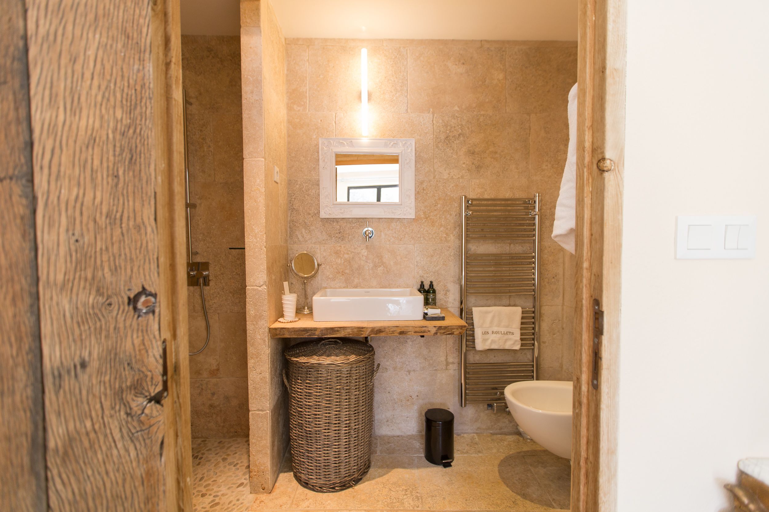Un baño con puerta de madera, un lavabo, un espejo, un perchero para toallas, un inodoro y un cubo de basura.