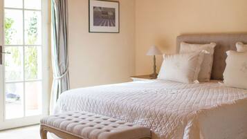 A bedroom with a large bed, a bench, a nightstand, and a window with curtains.