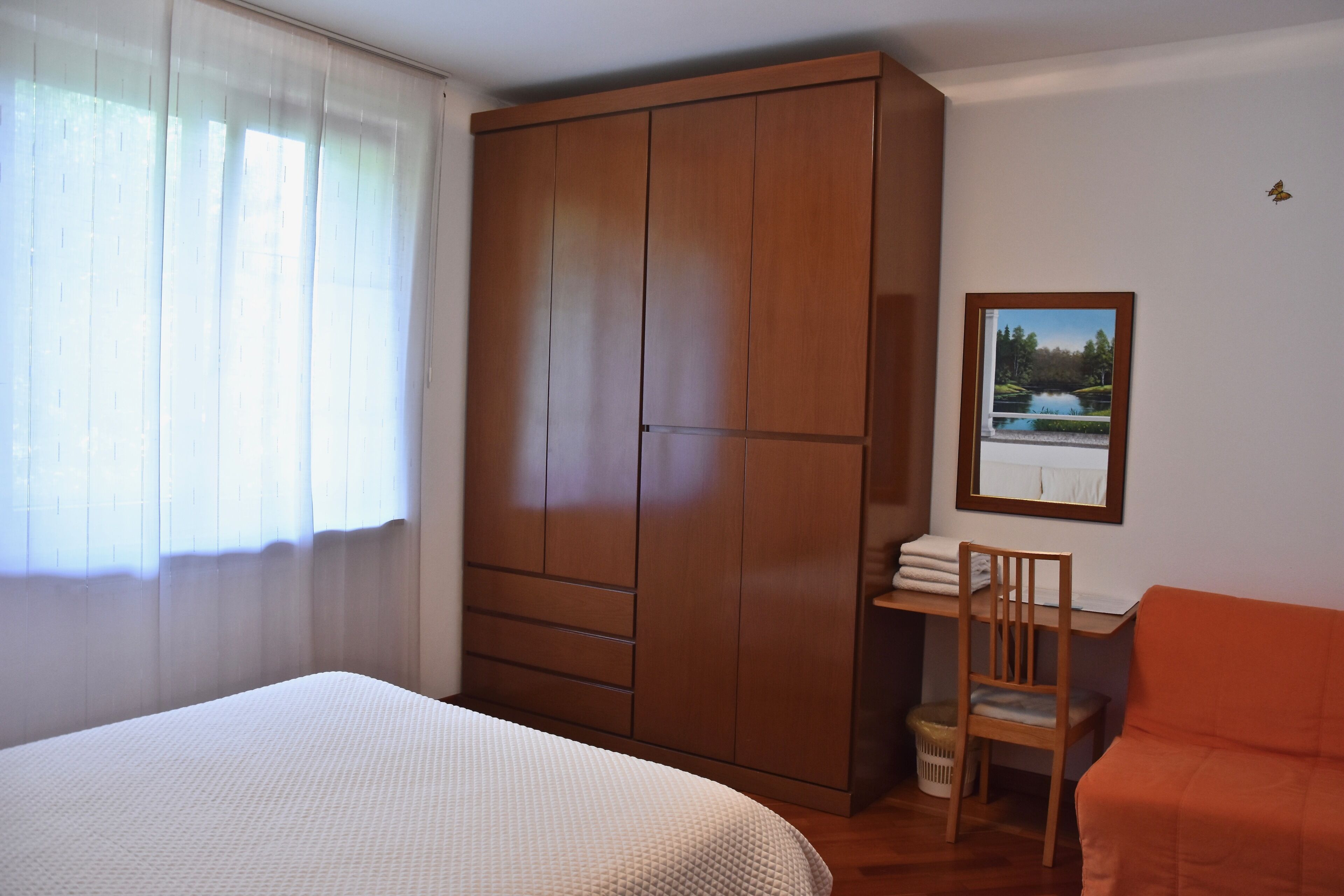 Une chambre à coucher comprenant un lit, une armoire, un bureau avec une chaise et un tableau encadré accroché au mur.