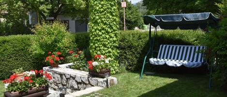 Un jardín con un banco de piedra, plantas en macetas y una pérgola.