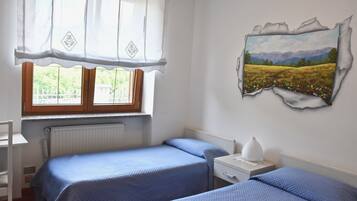 Une chambre avec deux lits, une fenêtre avec des rideaux, un radiateur, une table de chevet et un tableau accroché au mur.