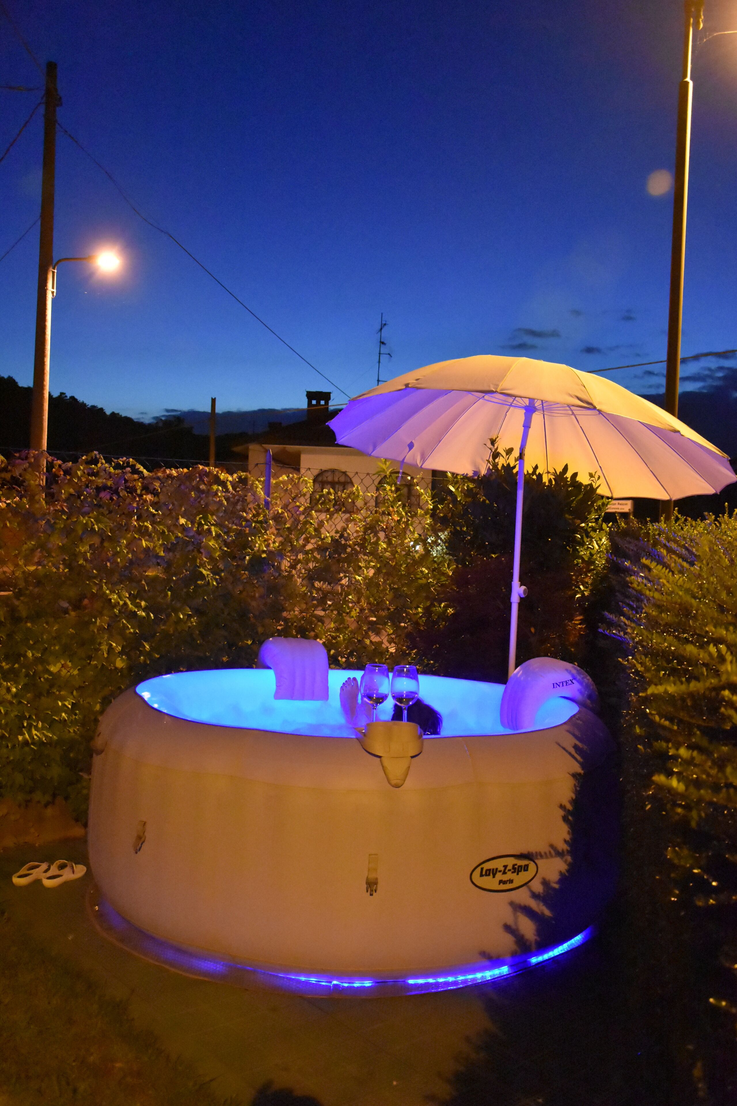 Un jacuzzi inflable con un paraguas amarillo, rodeado de follaje.