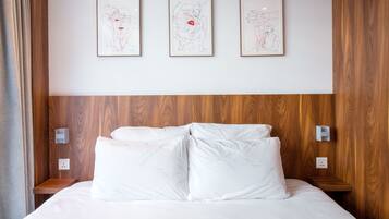 A hotel room with a large bed, wooden headboard, and three framed artworks on the wall.