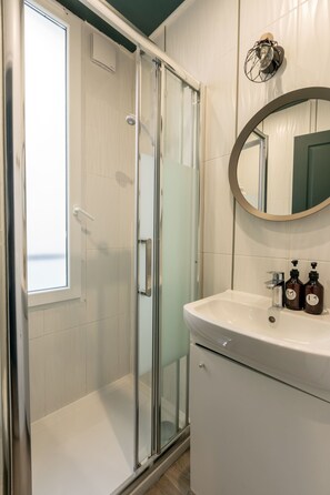 Un baño moderno con ducha envuelta en vidrio, un lavamanos blanco y un espejo redondo.