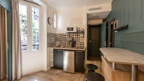 A compact kitchen with a microwave, sink, and a small refrigerator. There is a window with curtains, a clock on the wall, and a patterned backsplash. - HOTEL MAAT ETOILE (Paris)