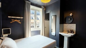 A hotel room with a bed, a bedside table, a mirror, a window with curtains, a wall-mounted TV, and a bathroom with a sink and mirror. - HOTEL MAAT ETOILE (Paris)