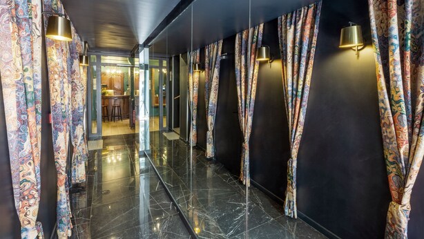 A hallway with patterned curtains, a reflective floor, and wall-mounted lights. - HOTEL MAAT ETOILE (Paris)