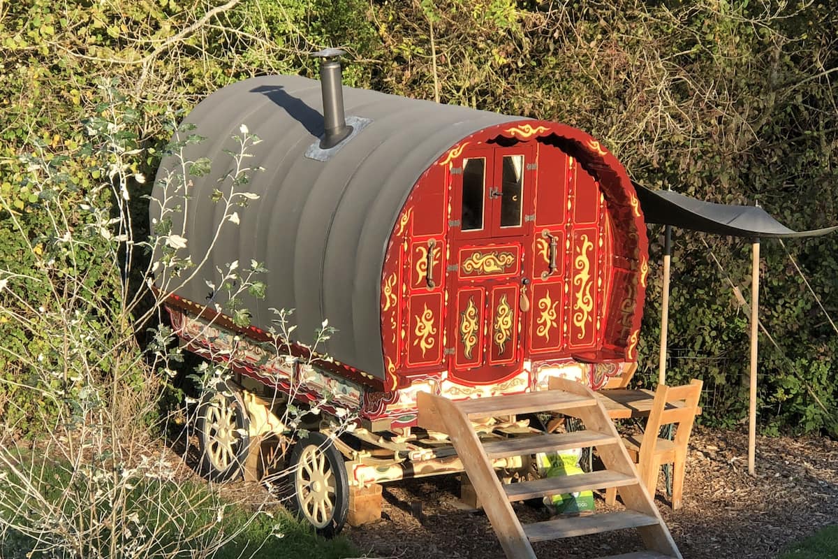 Een stilstaande treinwagon met een rode buitenkant en decoratieve gouden patronen, met een houten ladder die leidt naar een overdekt platform.