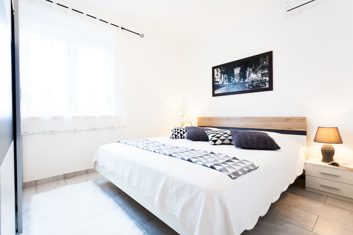 Quarto bem arrumado com uma cama grande, mesa de cabeceira com abajur e um quadro na parede.