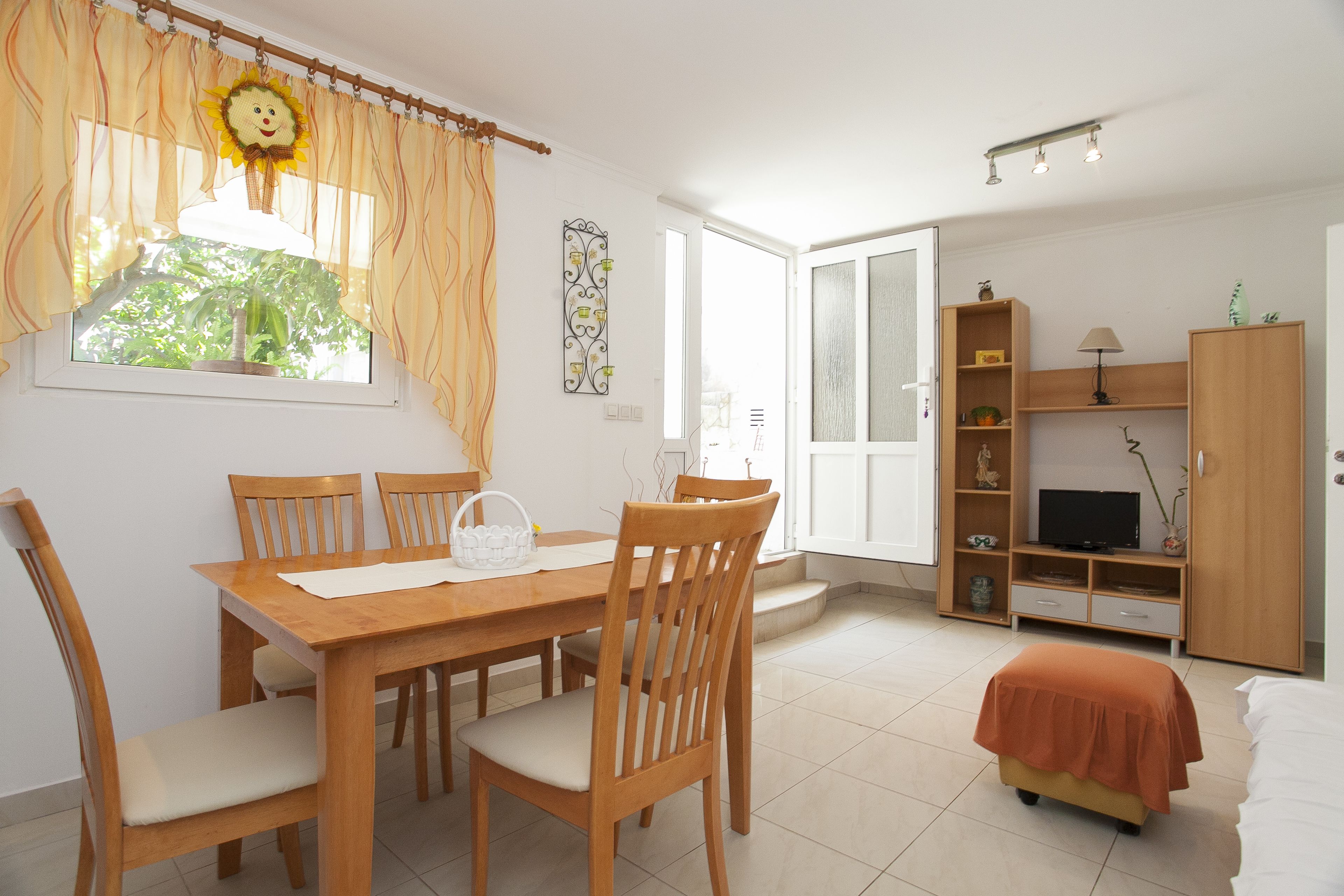 Un coin repas avec une table et des chaises en bois, un petit canapé et un téléviseur posé sur un meuble en bois.