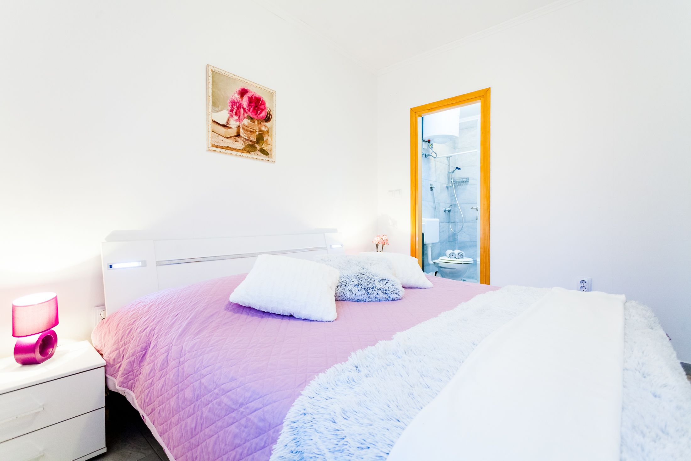 Une chambre à coucher avec un lit, une table de chevet, une lampe de chevet, un tableau encadré et une porte de salle de bain.