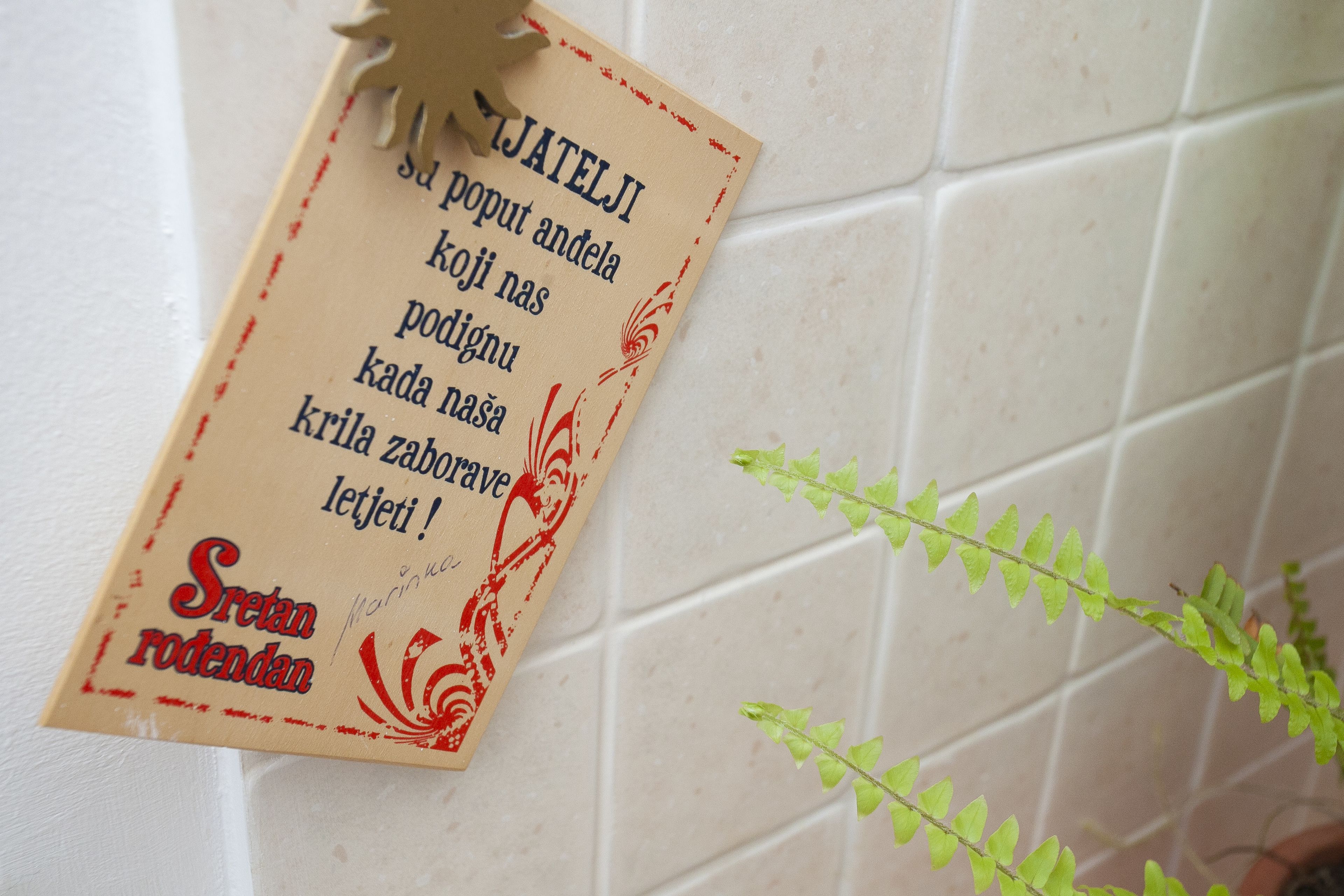 A handwritten sign with text in a non-English language, possibly a greeting or announcement, attached to a wall with a tiled pattern.