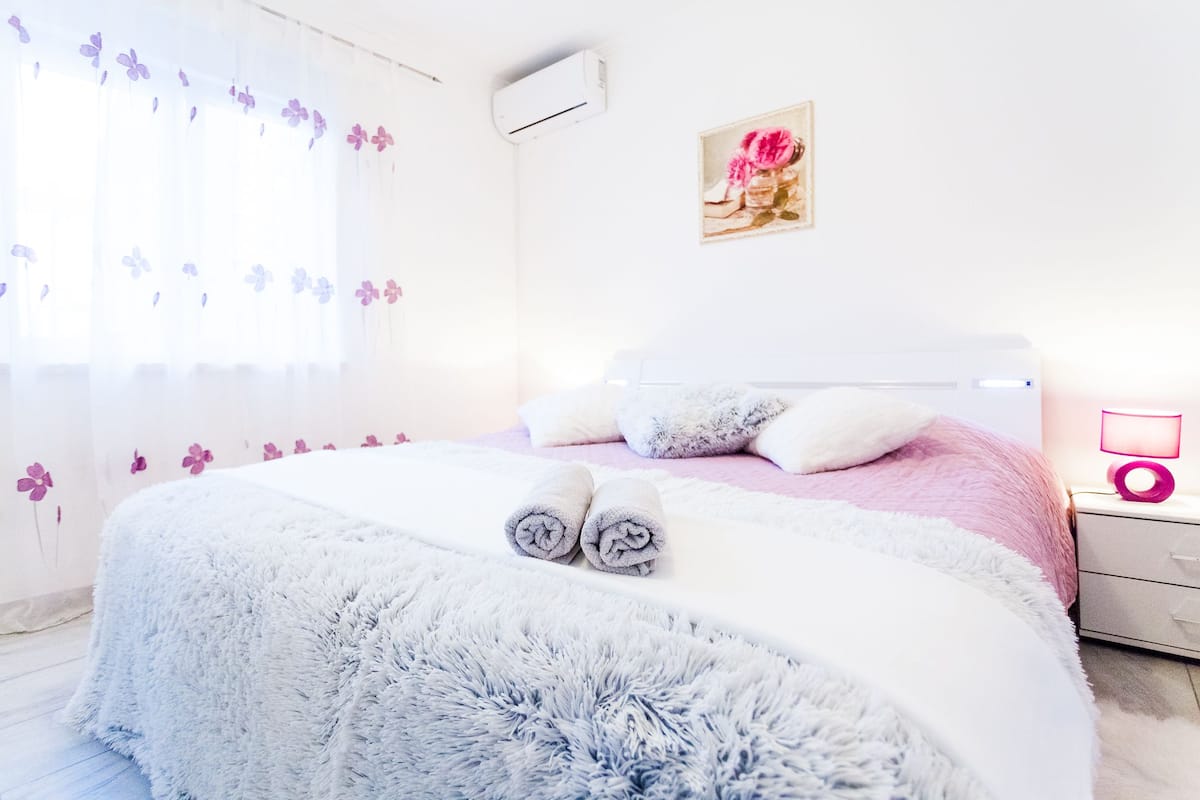 Cama bem arrumada com toalhas dobradas, abajur e ar-condicionado fixado na parede.