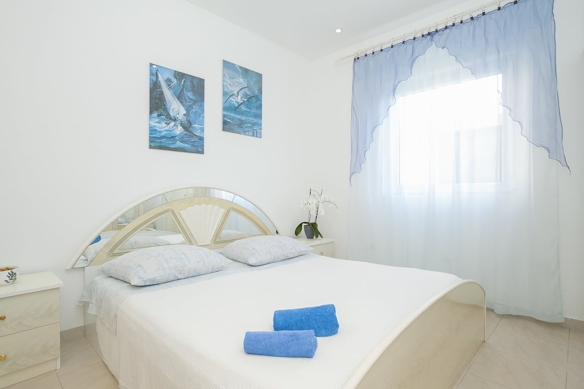 Quarto com cama, mesa de cabeceira, espelho e duas pinturas na parede.
