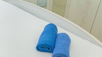 Dos toallas azules enrolladas sobre una superficie blanca con textura, posiblemente una cama o sofá, en una habitación con paneles de madera clara.