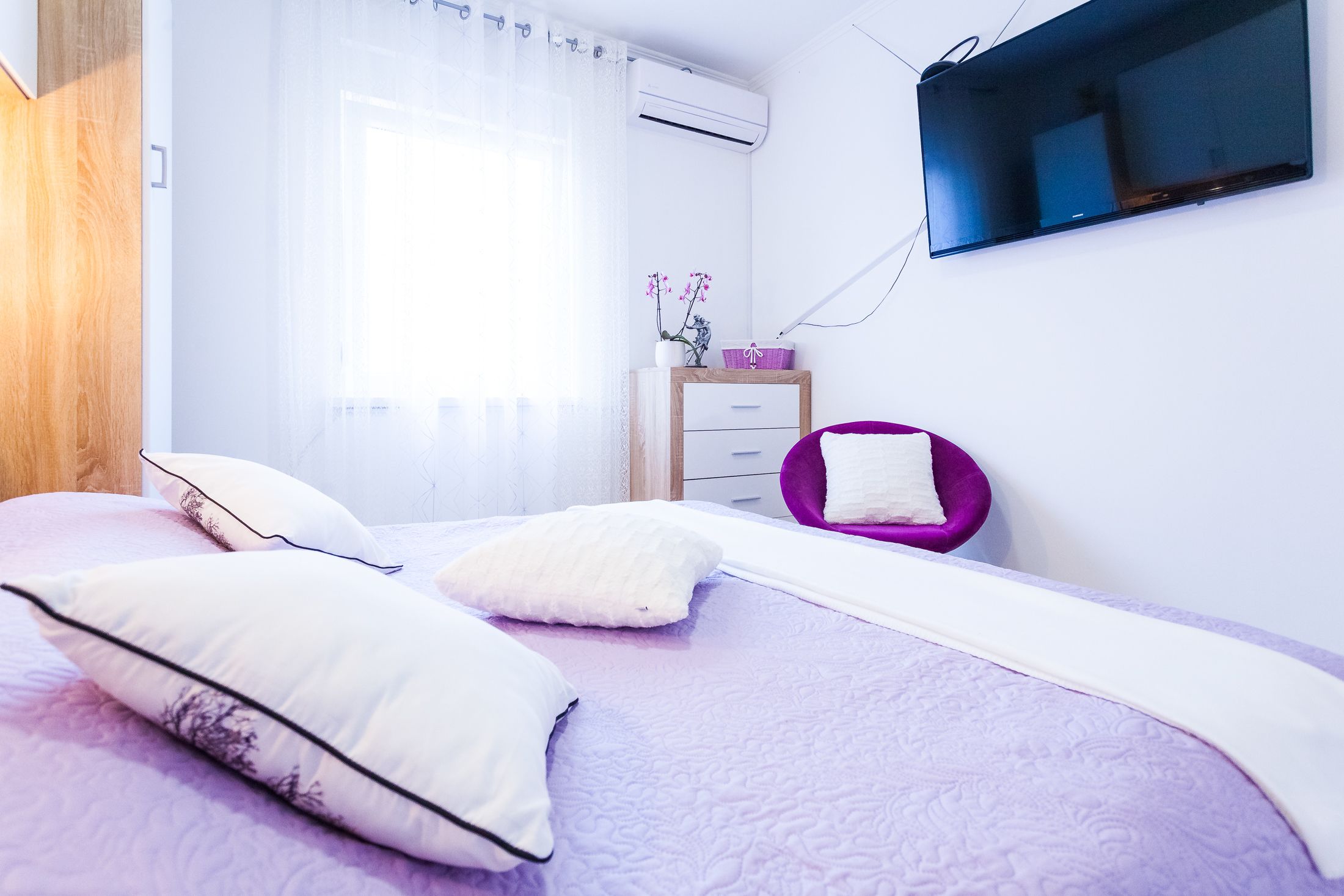 Ein modernes Schlafzimmer mit einem Bett, Kissen, einem Schminktisch, einer Kommode und einem an der Wand montierten Fernseher.