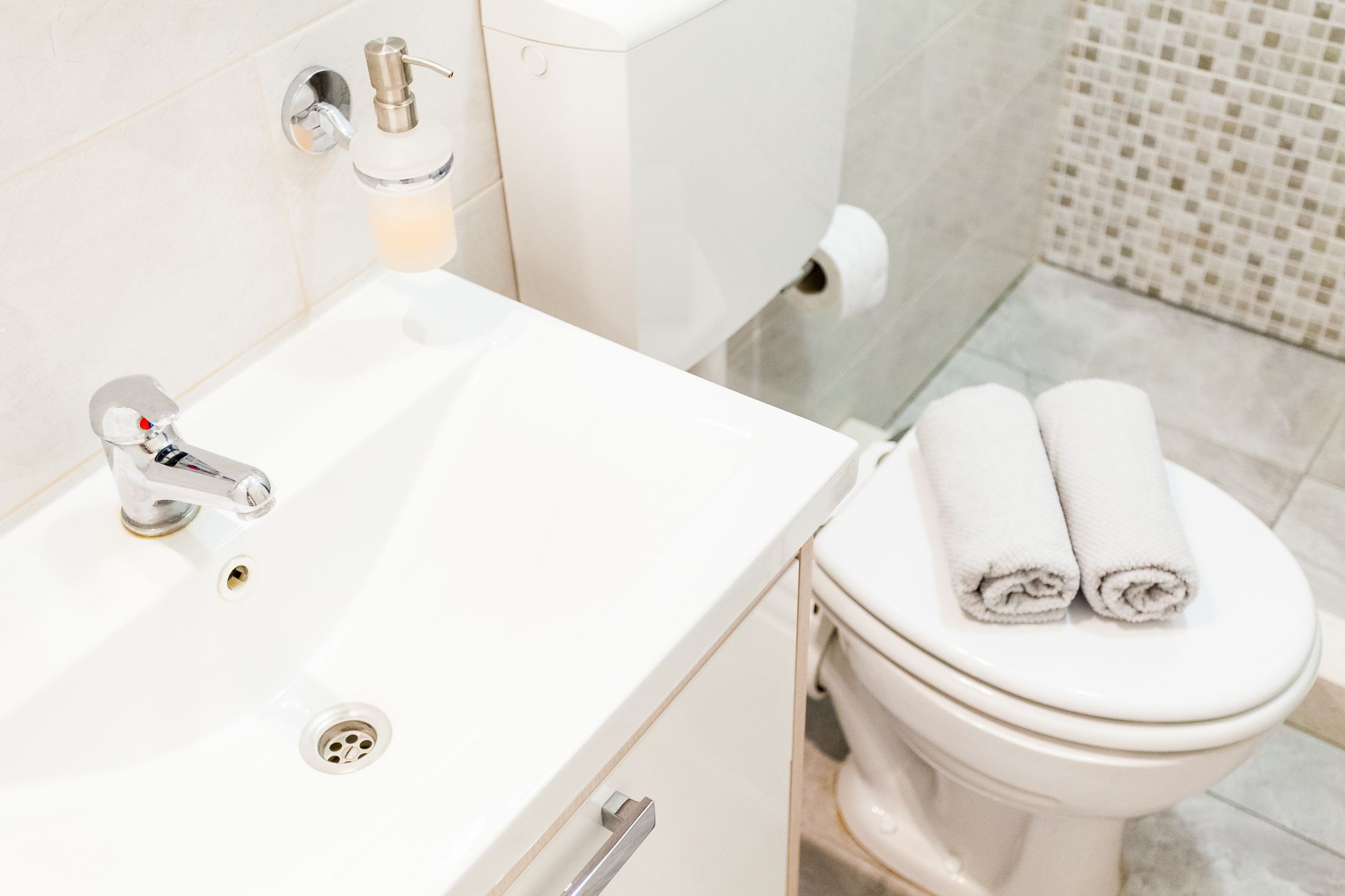 A bathroom with a white sink, a toilet, and a roll of toilet paper on the floor.