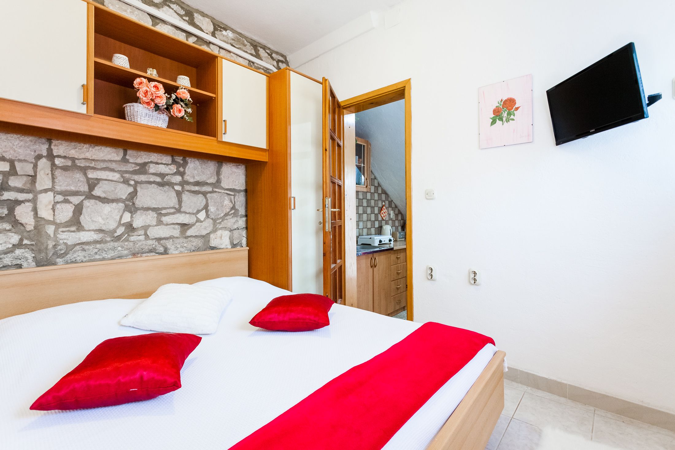 A bedroom with a bed, a wooden headboard, a stone wall, a TV, and a staircase.