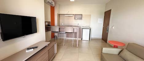 Una sala de estar moderna con un televisor de pantalla plana, un mueble de entretenimiento de madera, un sofá color beige y una mesita roja.