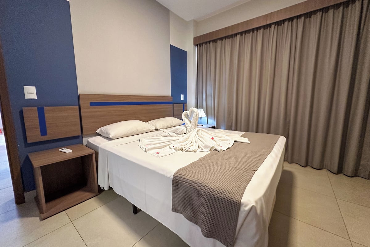 Ein Hotelzimmer mit einem Bett, einem Nachttisch, einer Lampe und einem Fenster mit Vorhängen.