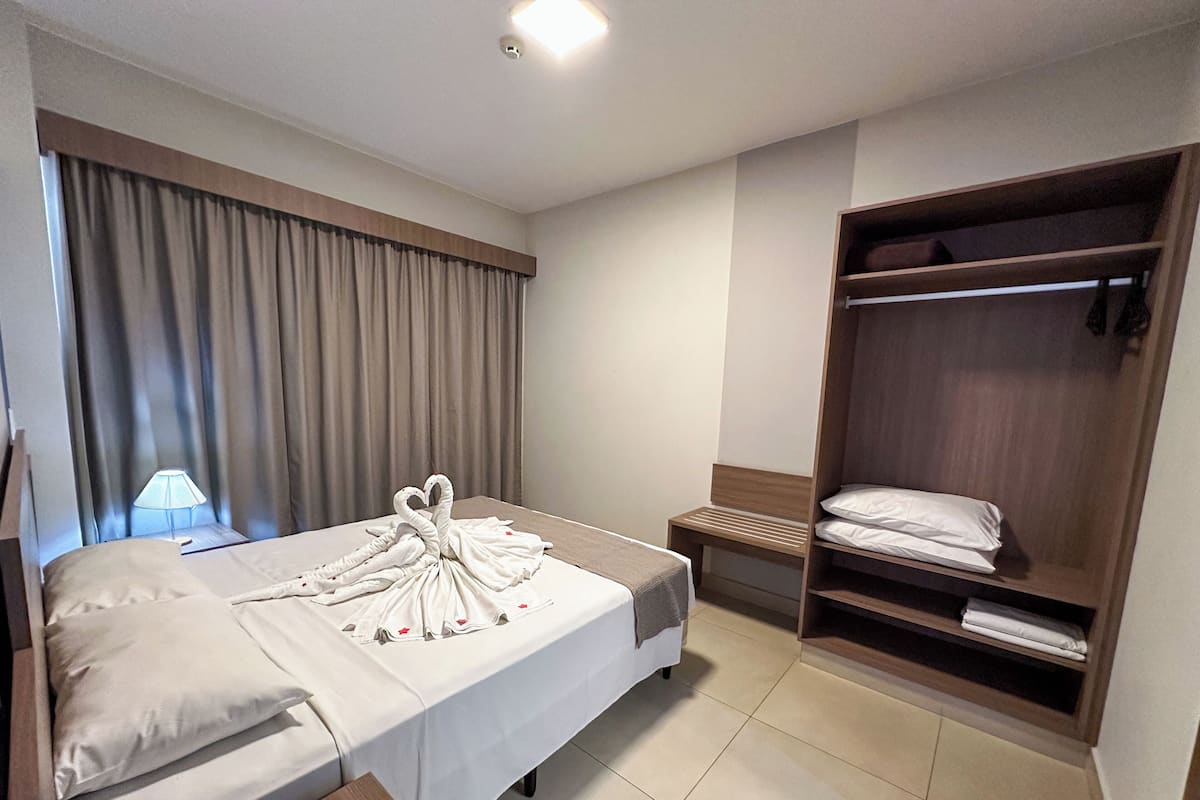 Ein Hotelzimmer mit einem Bett, einem Nachttisch mit Lampe, einem Holzschrank und einem Fenster mit Vorhängen.