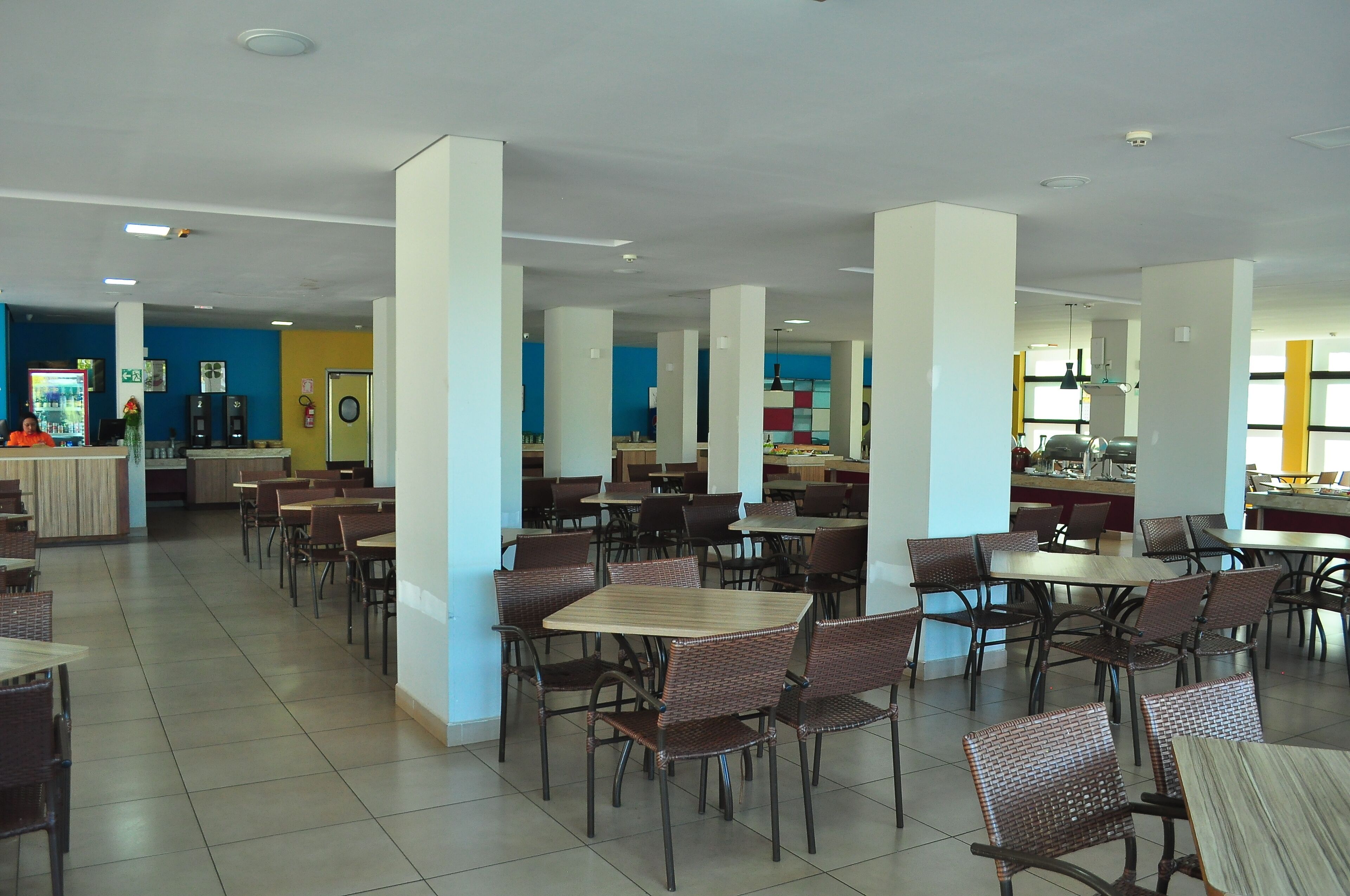 A spacious indoor dining area with multiple tables and chairs, a kitchen in the background, and a vending machine.