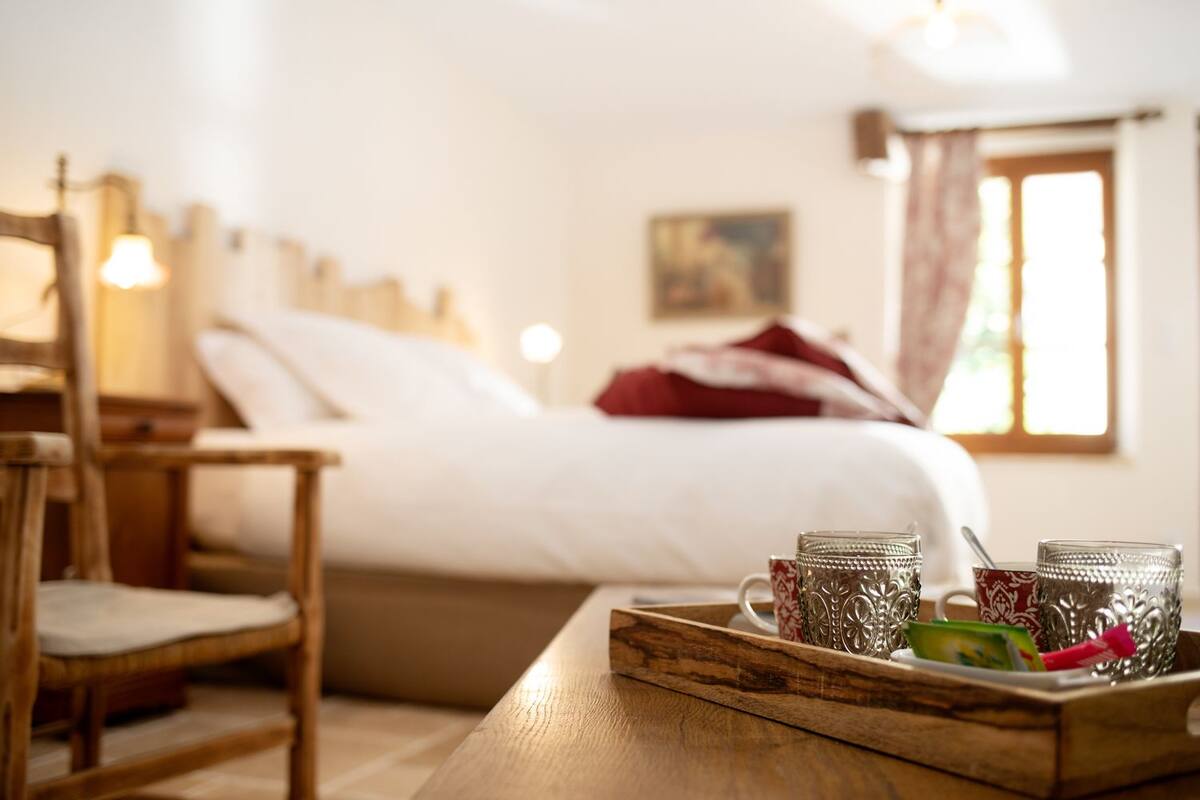 Una habitación de hotel acogedora con una cama de madera, una mesita de noche con una bandeja de vasos y una silla.