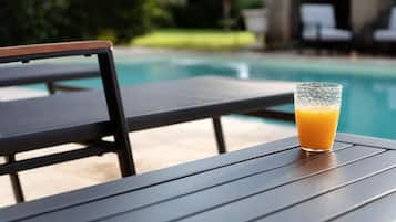 A glass of orange juice on a table by a poolside.