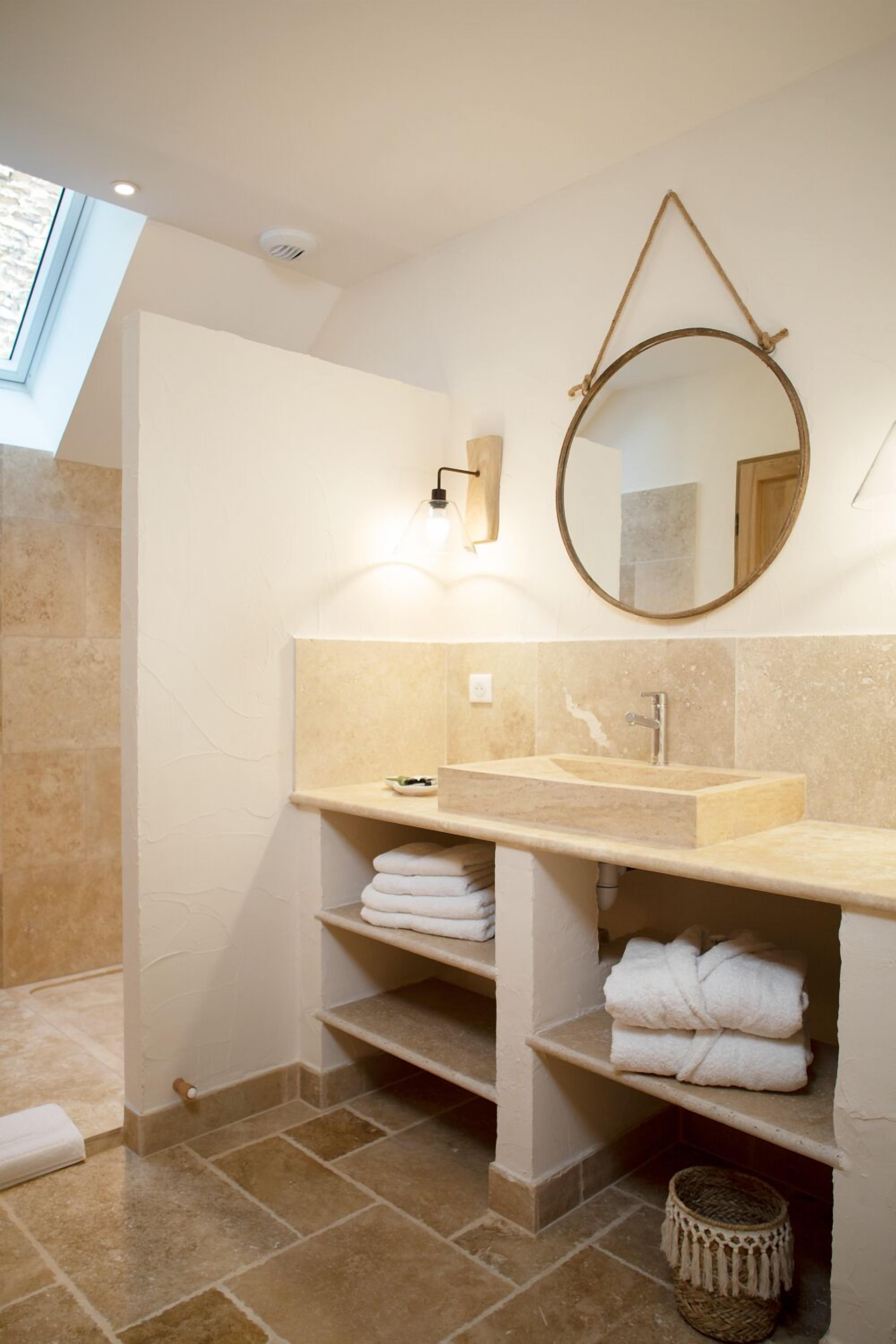 A bathroom with a large sink, a mirror, and shelves with towels.