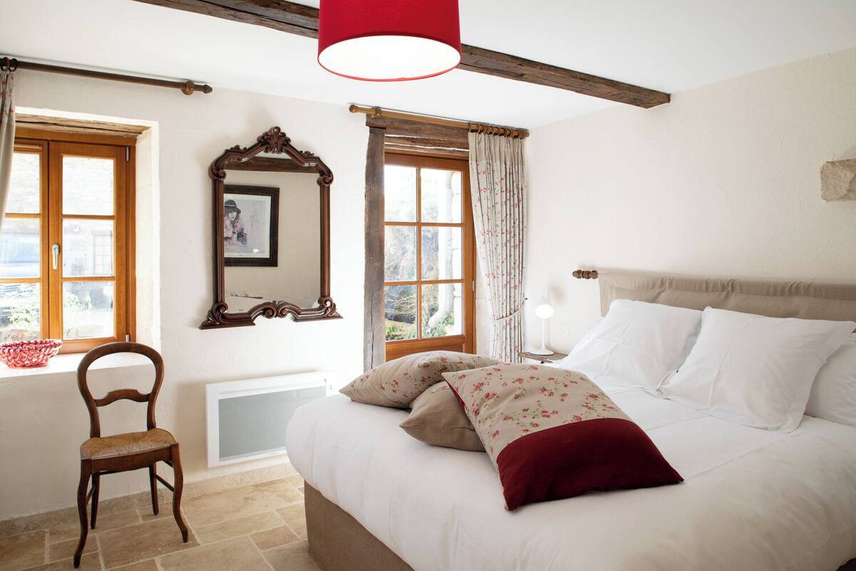 Un dormitorio con cama, una silla, ventana y espejo.