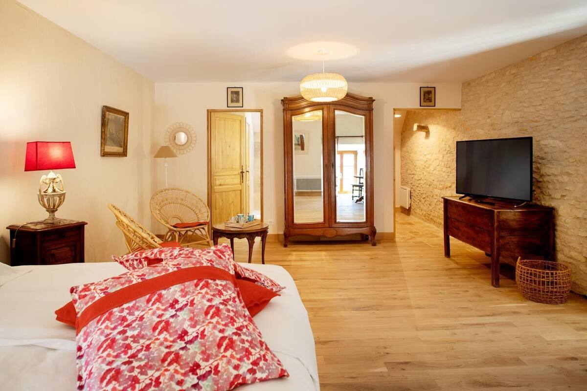 Una habitación de hotel con una cama, un televisor, un tocador de madera, una silla de mimbre, un espejo y una puerta que da a otra habitación.